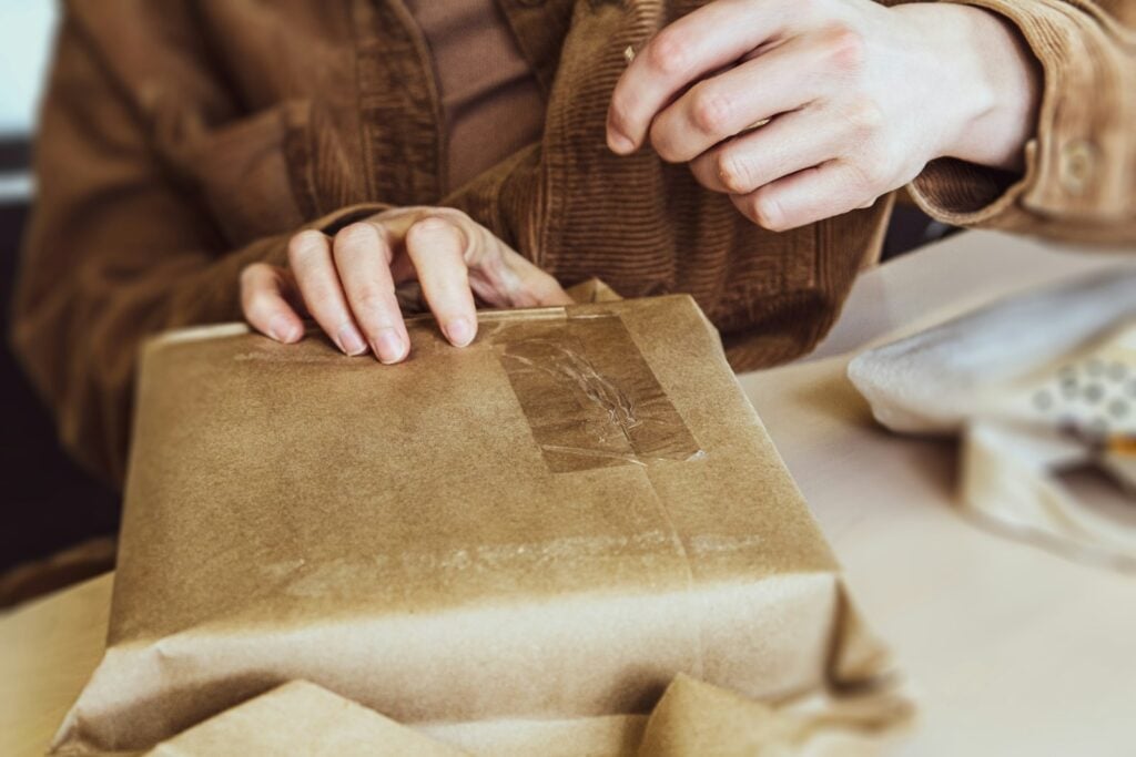 Hands holding a brown-paper parcel secured with clear tape.