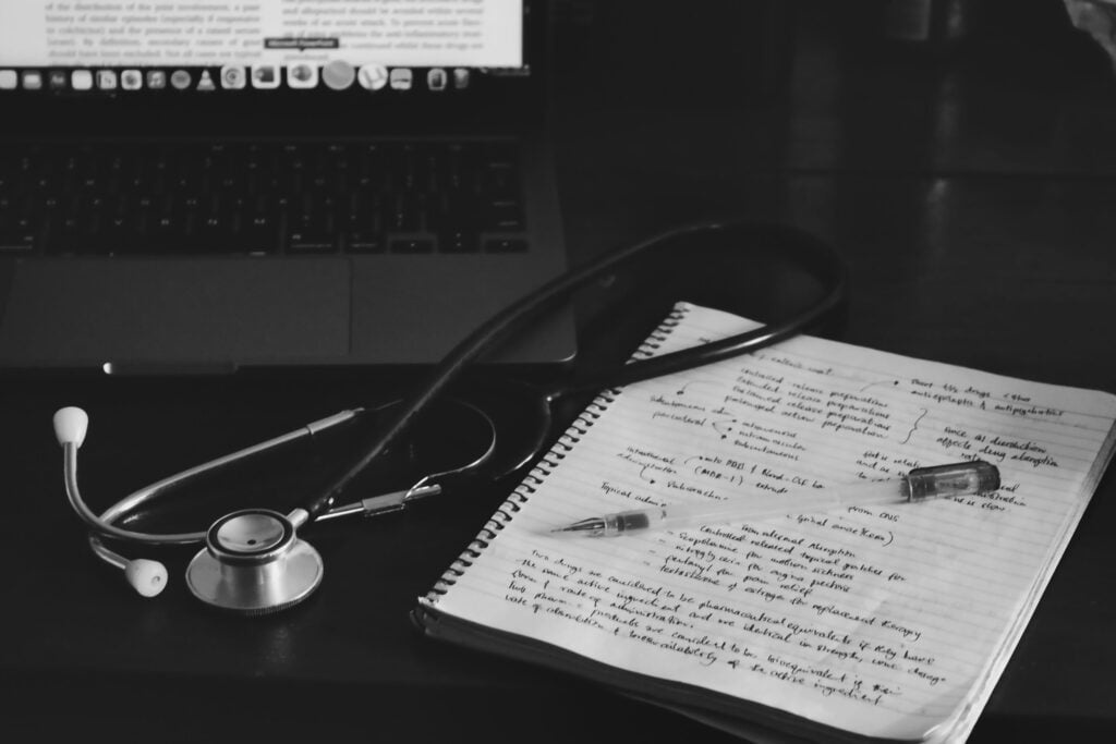 A stethoscope, open handwritten notebook and pen beside a laptop.