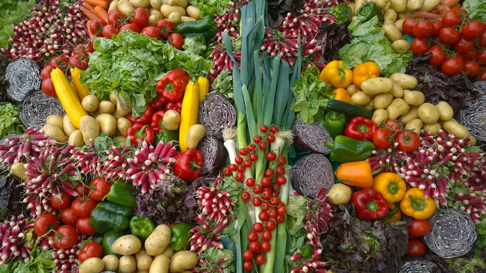 Display of peppers, tomatoes, potatoes, radishes and leafy vegetables.